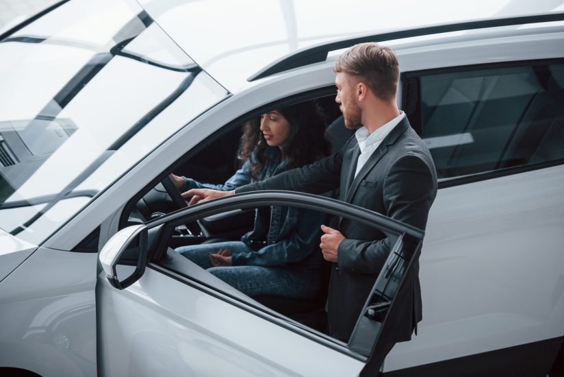 Helping girl to decide. Female customer and modern stylish bearded businessman in the automobile saloon.
